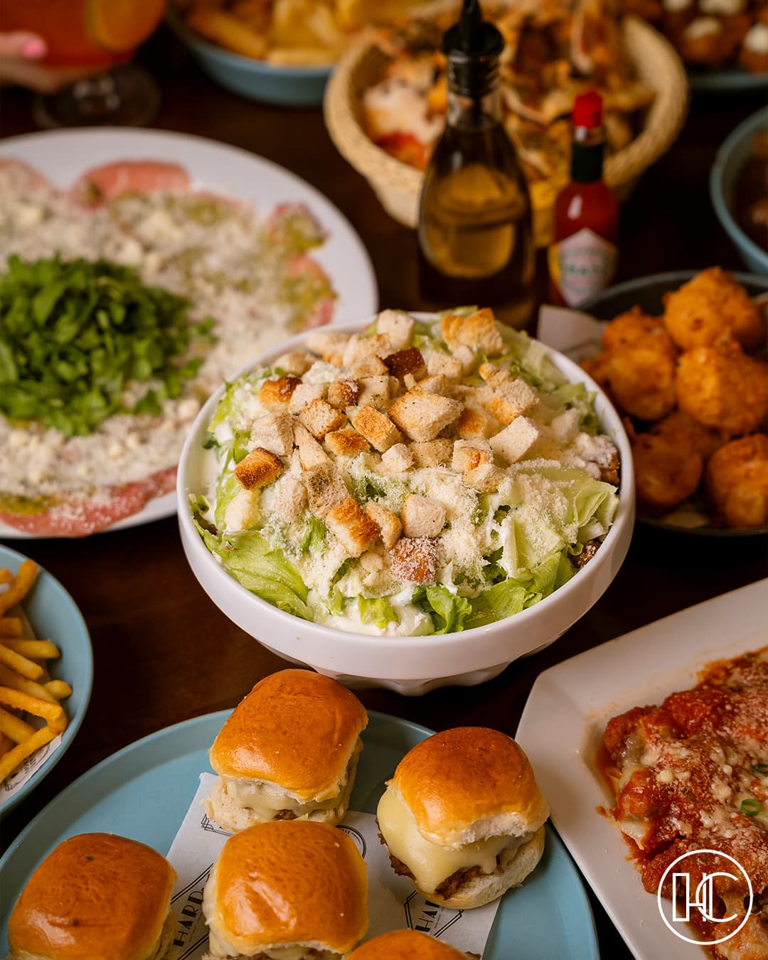 Salada Caesar, mini burgers e petiscos na mesa