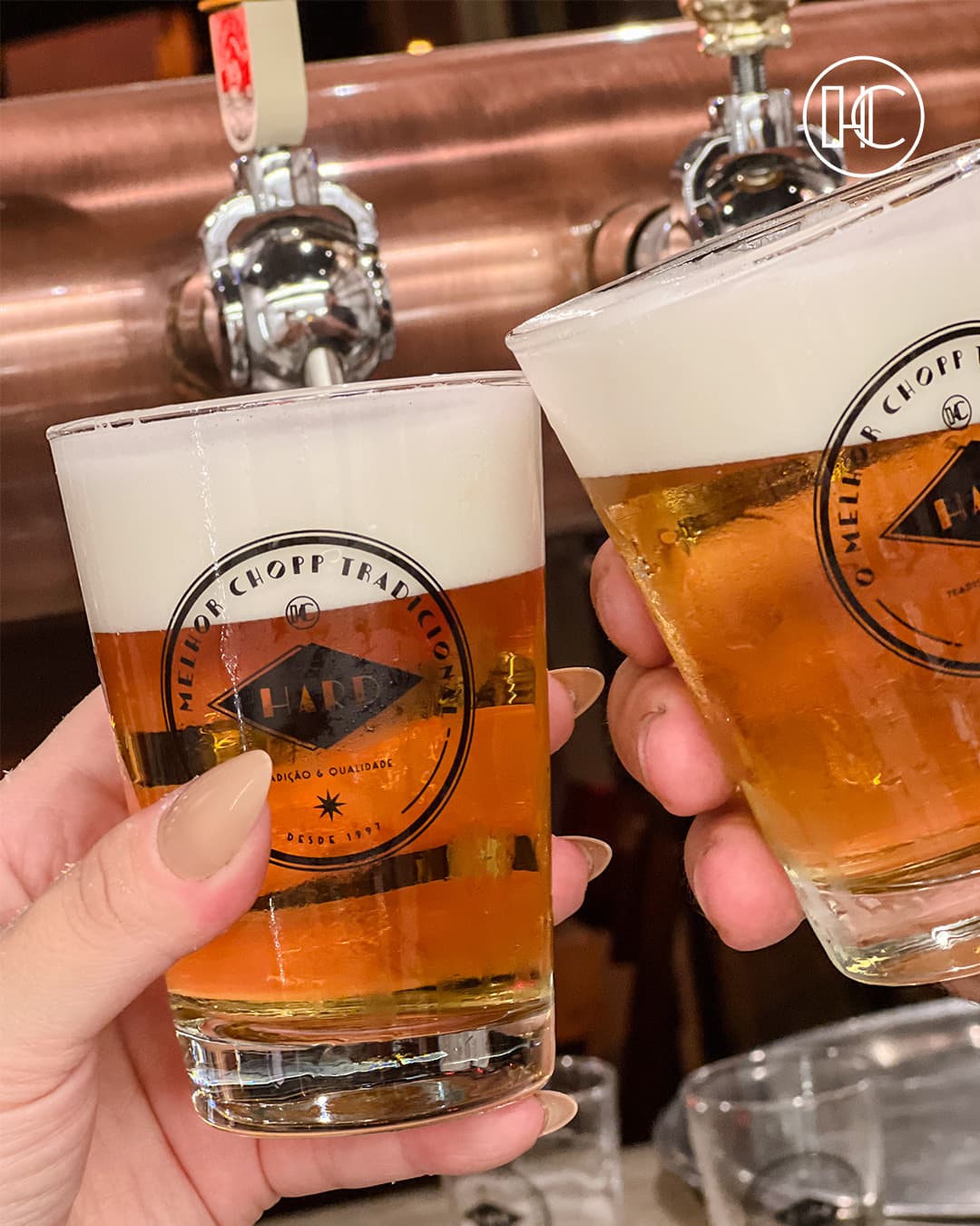 Dois copos de chopp com o losango da casa sendo servidos na chopeira