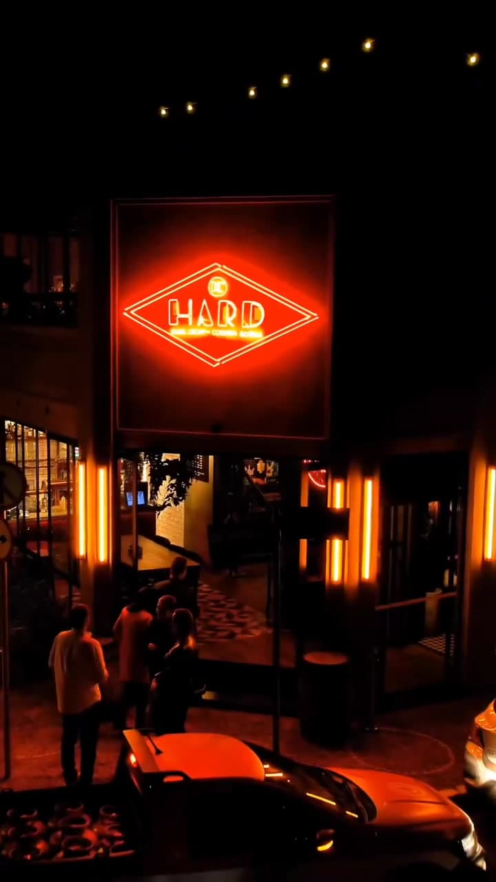 Fachada do Hard Chopp 2 à noite, com o losango de neon aceso sobre a porta