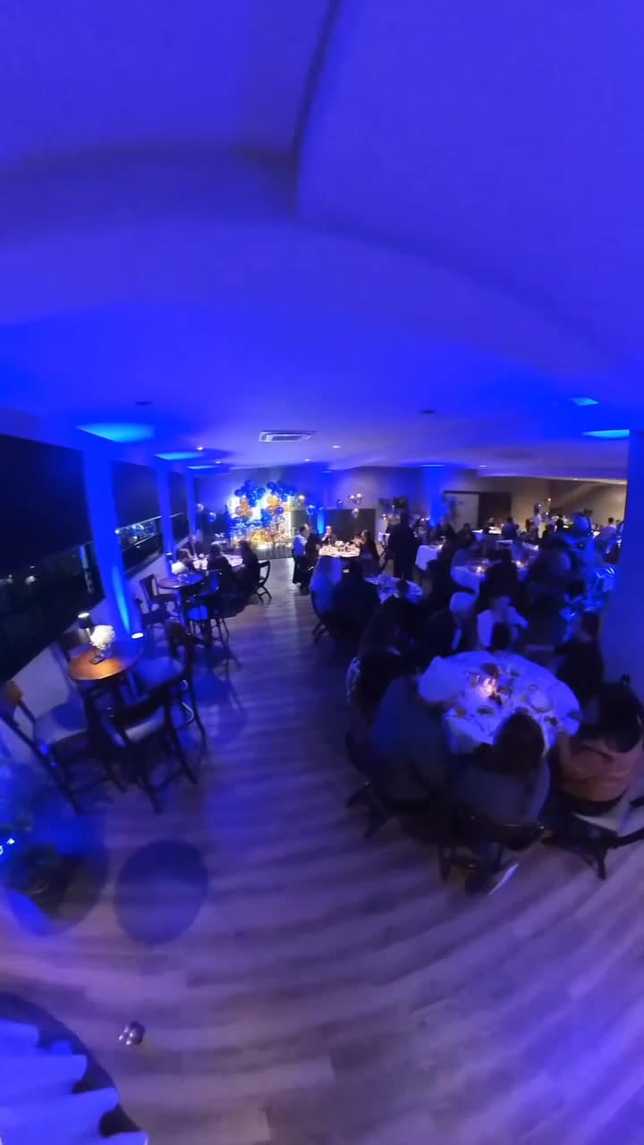 Salão fechado de eventos com mesas de toalha branca e luz azul