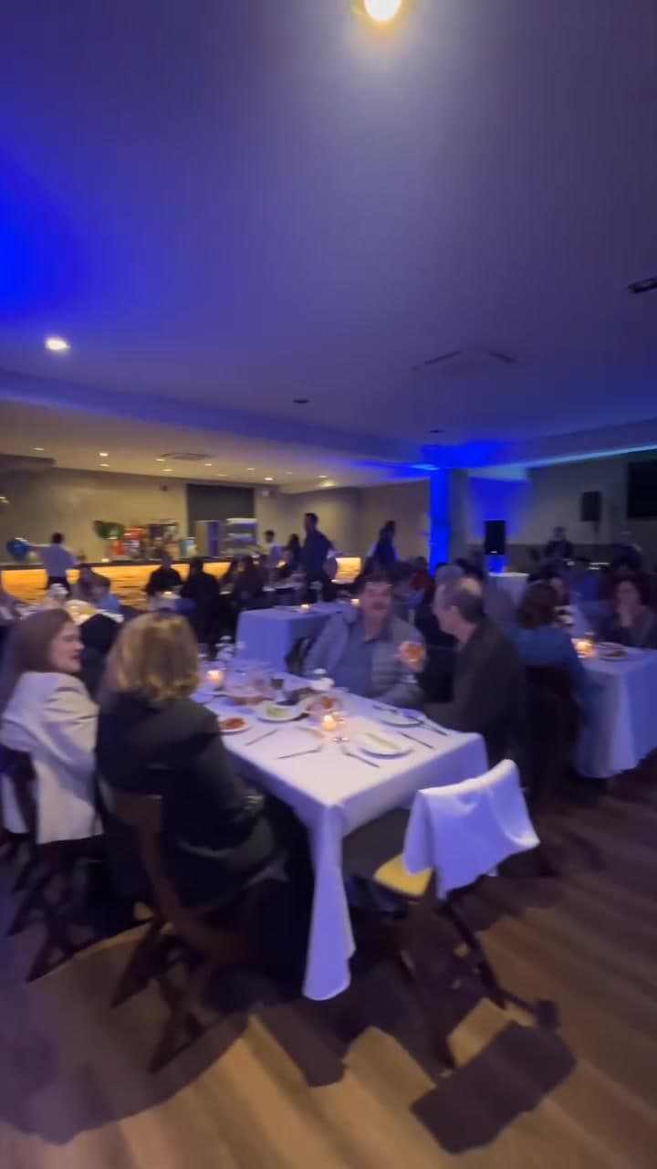 Salão fechado de eventos com mesas de toalha branca e luz azul
